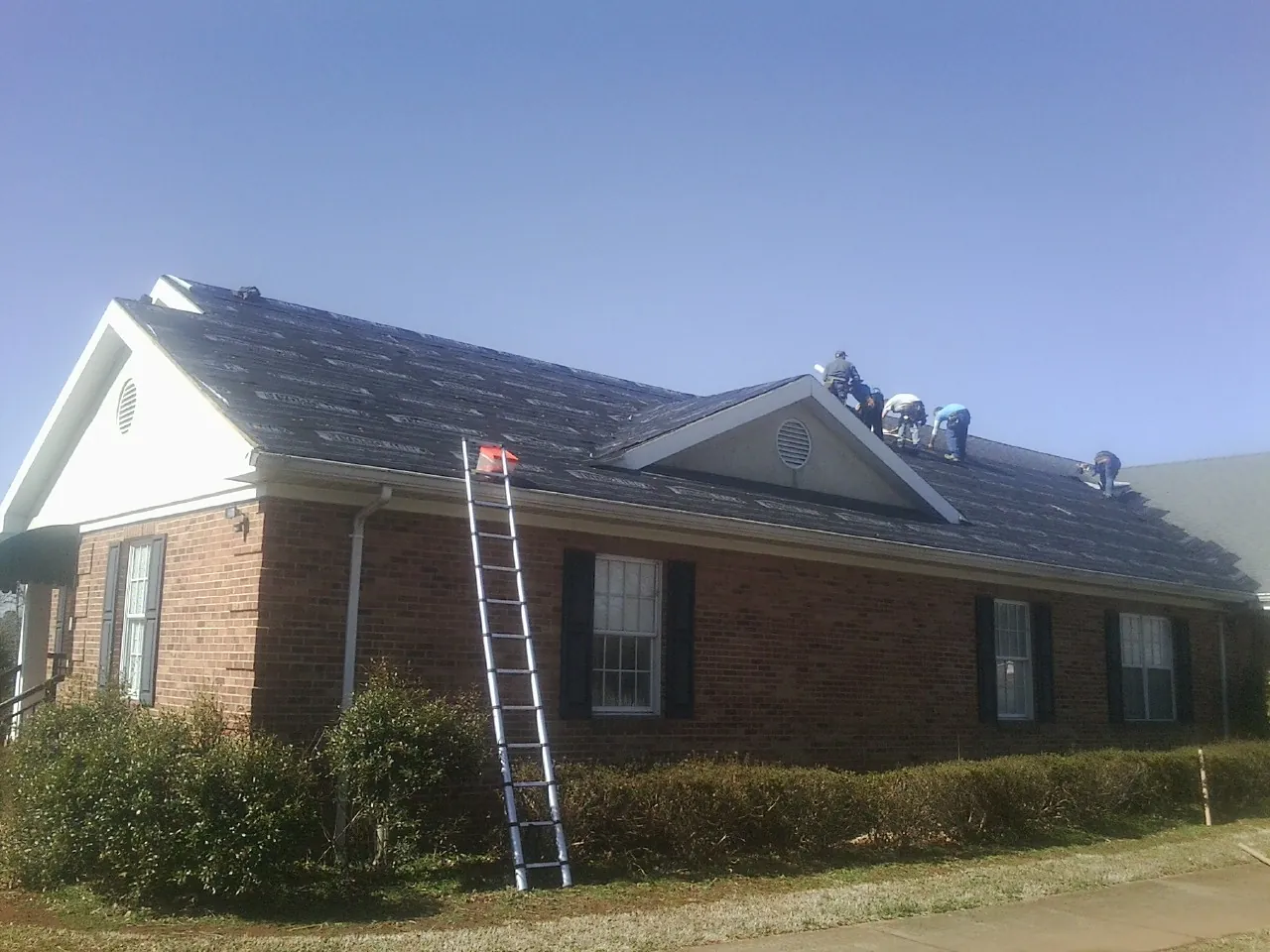 Crew tearing shingles off a brick ranch roof with a ladder set — Emergency Roof Repair work by our crew in Fairview Heights