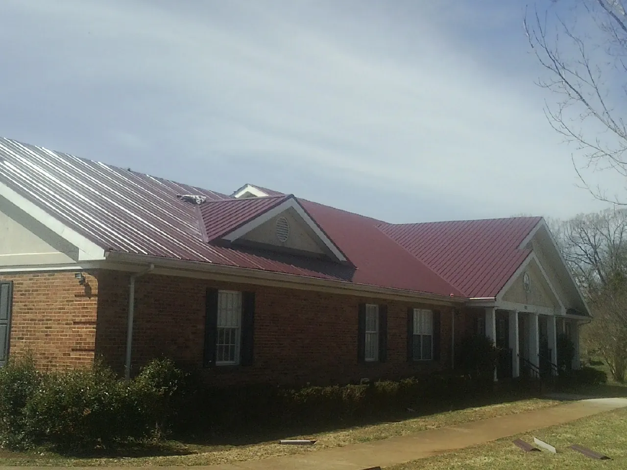 Red metal roof with gabled entries on a long brick building, from a Hail Damage Roof Repair job in Fairview Heights
