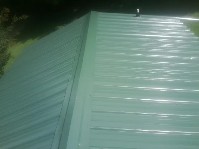 New green metal panels meeting at the ridge of a roof — Flat Roof Repair work by our crew in Fairview Heights