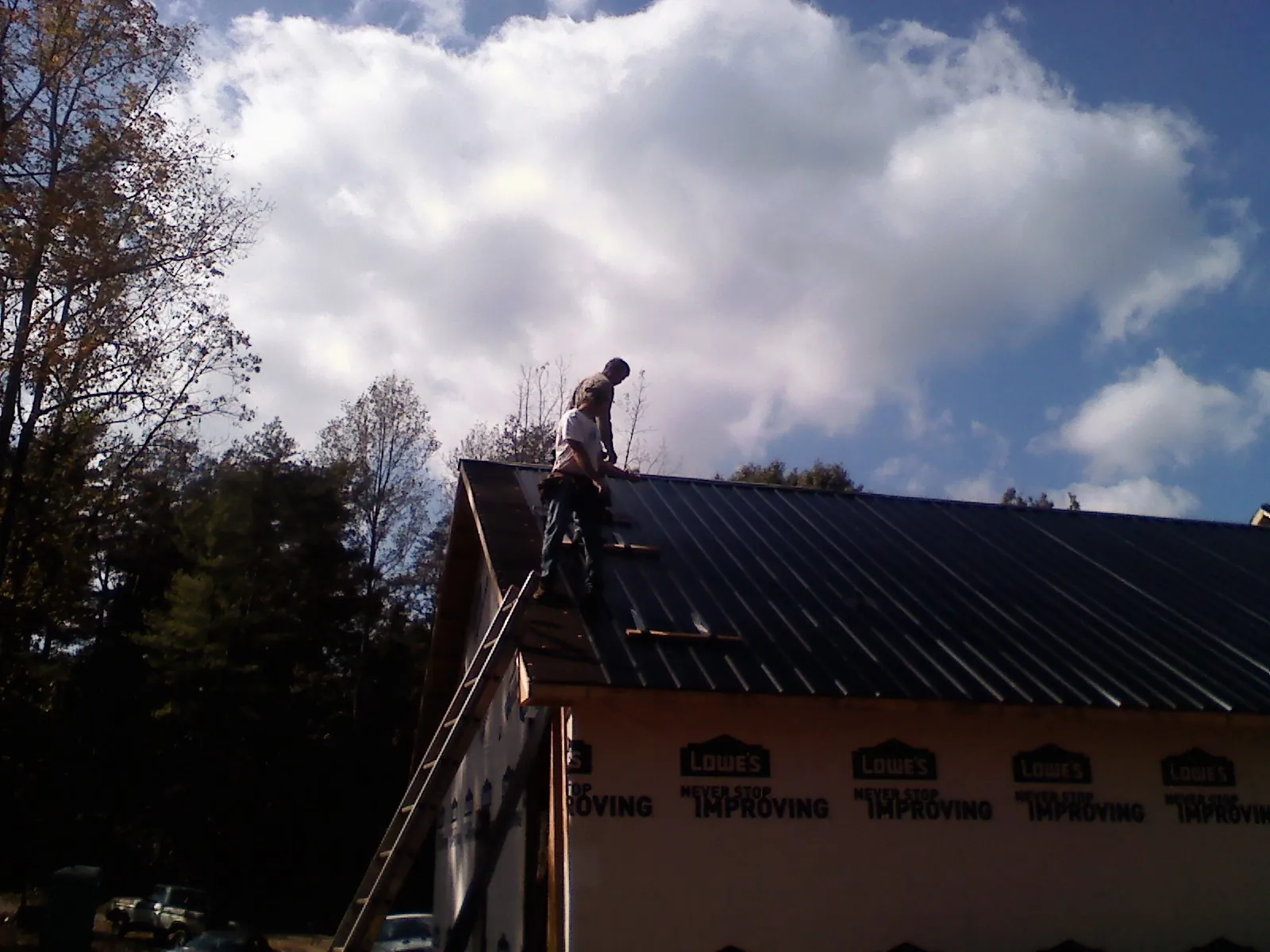 Roofer fastening dark metal panels high against a cloudy sky, from a Roof Inspection job in Fairview Heights