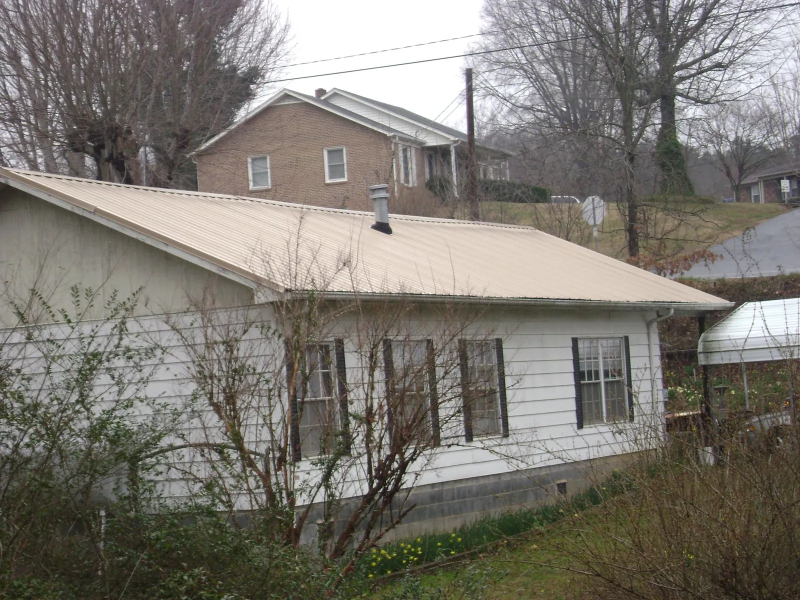 Tan metal roof on a white sided house set into a hillside — Commercial Roofing by Roofing Brothers in Fairview Heights