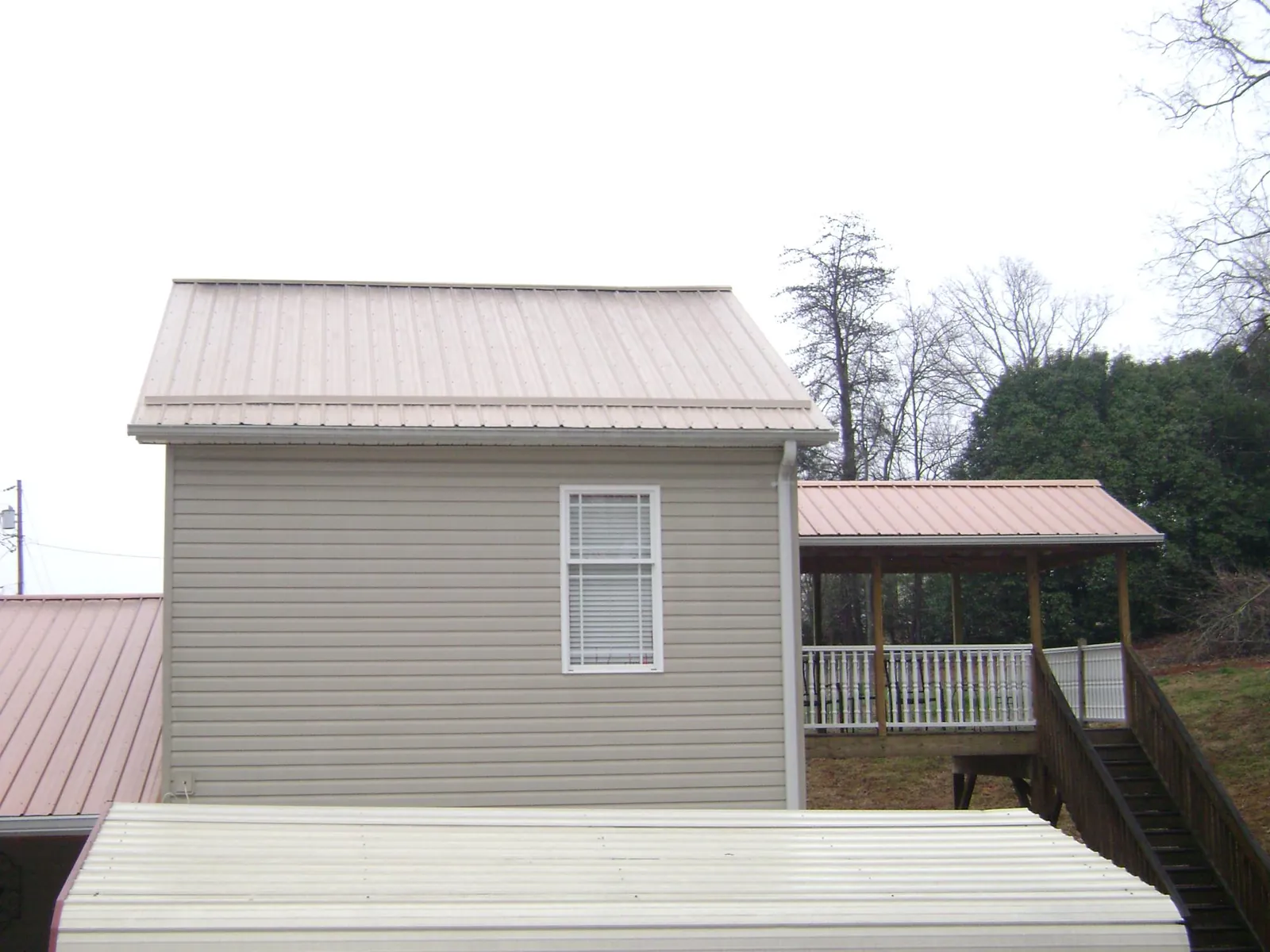 Tan metal roofs on a two story addition and attached porch, from a Roof Replacement job in Fairview Heights